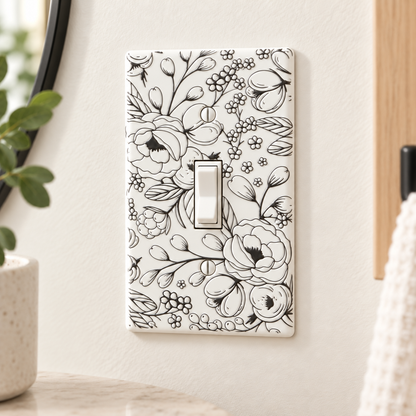 A single-toggle light switch plate with a black floral line-art pattern on a white background, mounted on a beige wall in a styled interior setting.