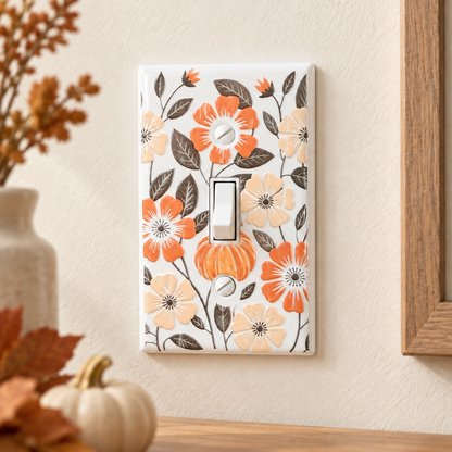 A single light switch plate cover with a white background and a floral pattern of orange, peach, and brown flowers with dark brown leaves, shown mounted on a beige wall with decorative pumpkins and a vase in the foreground.